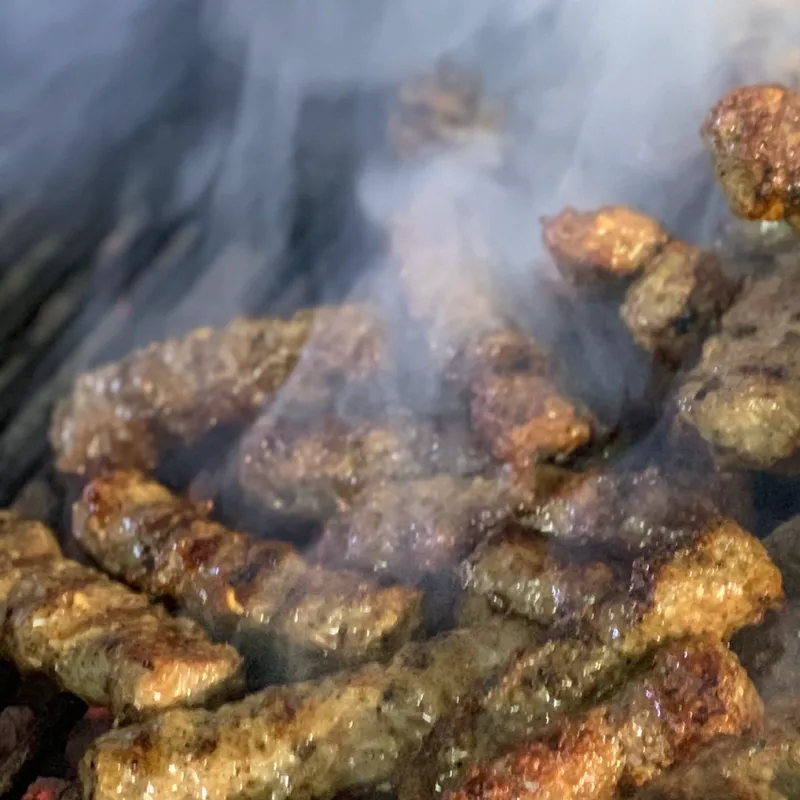 Cevapcici som grillas på en grill och rök.