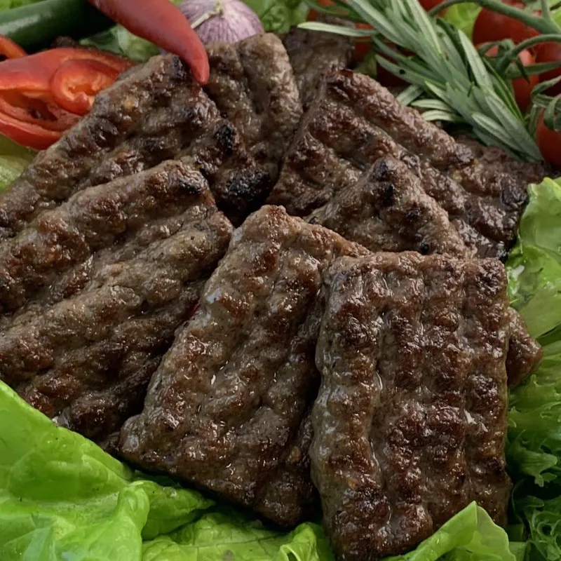 Cevapcici i sallad med tomater och grönsaker runtomkring.